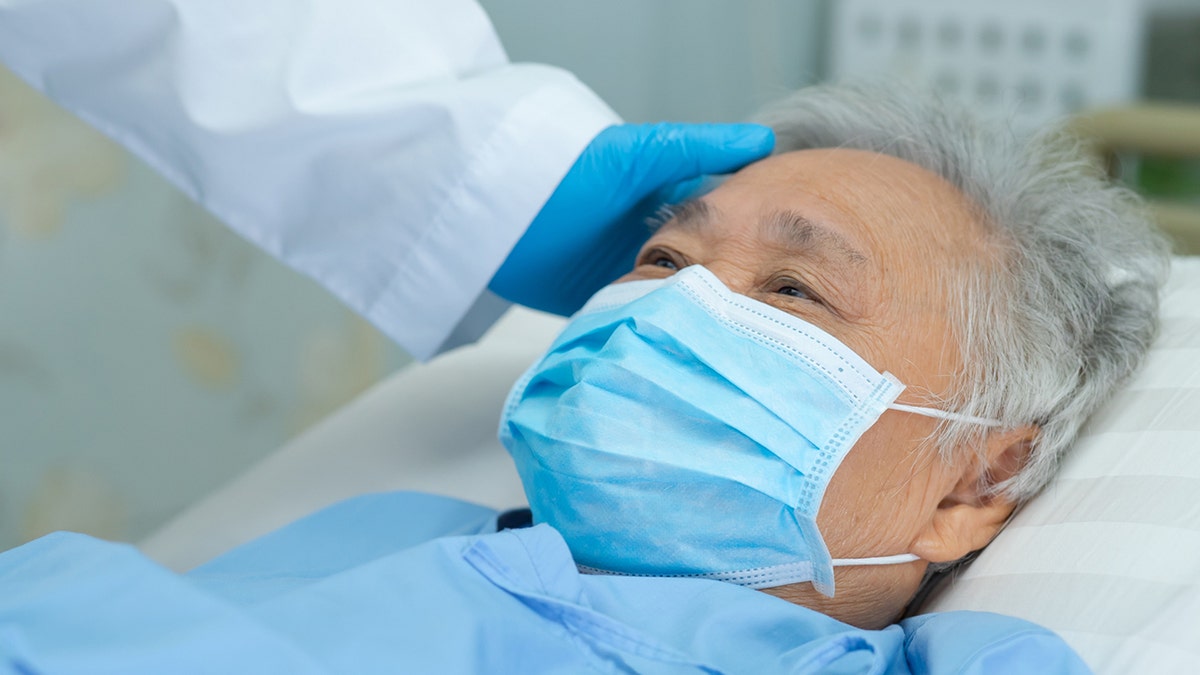 Doctor touching and checking Asian senior or elderly old lady woman patient wearing a face mask in hospital for protect infection and kill Novel Coronavirus (2019-nCoV)