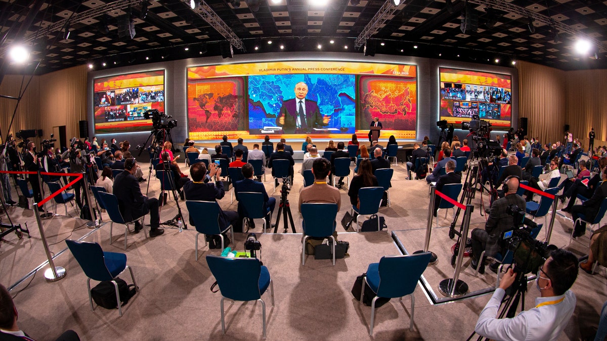 Russian President Vladimir Putin gestures as he speaks via video call during a news conference as journalists wearing face masks to protect against coronavirus, observe social distancing guidelines watch him at a big screen in Moscow, Russia, Thursday, Dec. 17, 2020. This year, Putin attended his annual news conference online due to the coronavirus pandemic. (AP Photo/Alexander Zemlianichenko)