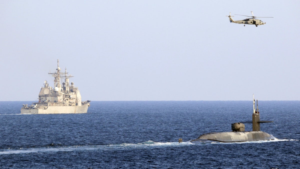 The guided-missile submarine USS Georgia, right, transits the Strait of Hormuz with the guided-missile cruiser USS Port Royal, the guided-missile cruiser USS Philippine Sea, not pictured, and an MH-60R Sea Hawk helicopter, attached to Helicopter Maritime Strike Squadron 48. (U.S. Navy photo by Mass Communication Specialist 2nd Class Indra Beaufort)