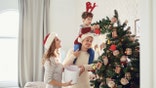 Mother, father and son in sweaters paint the Christmas tree in the house.