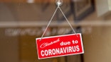 Red sign hanging at the glass door of a shop saying "Closed due to coronavirus".