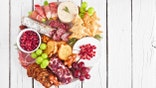 Christmas theme charcuterie board. Overhead view against a white wood background. Selection of cheese and meat appetizers.