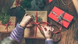 Young woman wrapping Christmas gifts on wooden table