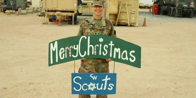 U.S. Army Spc. Anna Schmeck, automated logistical specialist with Headquarters Support Company, 628th Aviation Support Battalion, 28th Expeditionary Combat Aviation Brigade, poses for a photo at a motor pool in the 28th ECAB's area of operations in the Middle East. She made the sign for her students and colleagues at Conrad Weiser West Elementary School, where she works as a teacher.