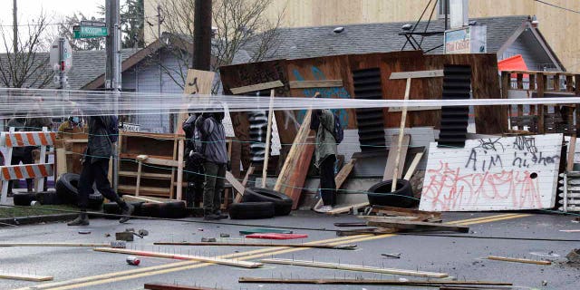 Protesters stand behind barricades at their encampment outside a home in Portland, Ore., on Wednesday, Dec. 9, 2020. Makeshift barricades erected by protesters are still up in Oregon's largest city a day after Portland police arrested about a dozen people in a clash over gentrification and the eviction of a family from a home. (AP Photo/Gillian Flaccus)