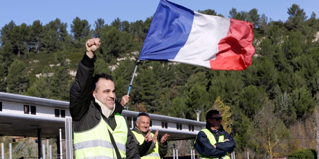 A demonstrators wearing a yellow vest clenches his fist as protesters open the toll gates on a motorway near Aix-en-Provence, southeastern France, Tuesday, Dec. 4, 2018. French Prime Minister Edouard Philippe announced a suspension of fuel tax hikes Tuesday, a major U-turn in an effort to appease a protest movement that has radicalized and plunged Paris into chaos last weekend. (AP Photo/Claude Paris)