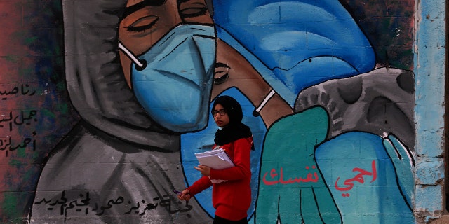 A student walks past a mural encouraging the wearing of face masks amid the coronavirus pandemic, on the main road of Nusseirat refugee camp, central Gaza Strip, 화요일, 11 월. 24, 2020. Arabic message reads: "Protect yourself." (AP Photo/Adel Hana)