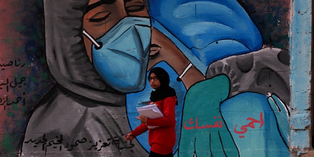 A student walks past a mural encouraging the wearing of face masks amid the coronavirus pandemic, on the main road of Nusseirat refugee camp, central Gaza Strip, Tuesday, Nov. 24, 2020. Arabic message reads: "Protect yourself." (AP Photo/Adel Hana)