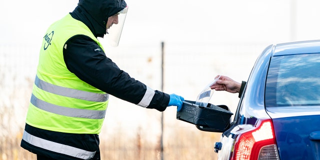 A man wearing a face shield is handed a COVID-19 self-test at a sampling site in a car park at Svågertorp station in Malmö, Sweden, Friday, Nov. 27, 2020. People with symptoms can perform the test on themselves in their vehicle. (Johan Nilsson/TT via AP)