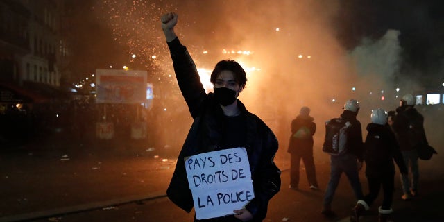 A protester holds a poster reading "Land of rights for the police" during a demonstration against a security law Saturday, Nov. 28, 2020 in Paris. Thousands of critics of a proposed security law that would restrict sharing images of police officers in France gathered across the country in protest, and officers in Paris who were advised to behave responsibly during the demonstrations fired tear gas to disperse rowdy protesters in the largely peaceful crowd. The cause has gained fresh impetus in recent days after footage emerged of French police officers beating up a Black man, triggering a nationwide outcry. (AP Photo/Francois Mori)