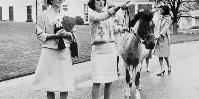 In this April 12, 1962, file photo first lady Jacqueline Kennedy gives a guided tour of the White House grounds to Empress Farah Pahlavi of Iran in Washington. Kennedy leads her daughter Caroline's pony, Macaroni, which had been nuzzling the empress, attracted by the daffodils she was carrying. (AP Photo/Pool)