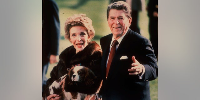This December 1986 file photo shows then-first lady Nancy Reagan holding Rex, a King Charles spaniel, as she and President Reagan walked on the White House South lawn. 