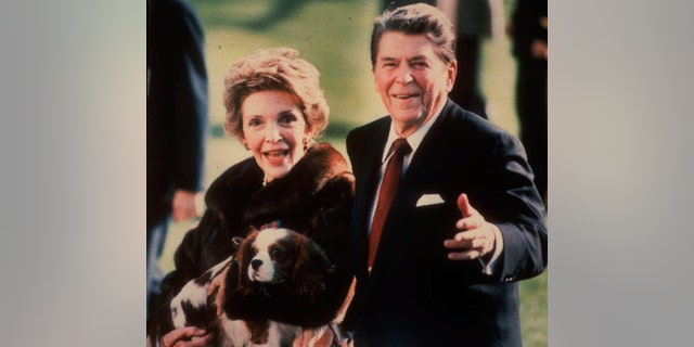 This December 1986 file photo shows the then-first lady Nancy Reagan holding Rex, King Charles Spaniel, as she walks on the grass south of the White House. 