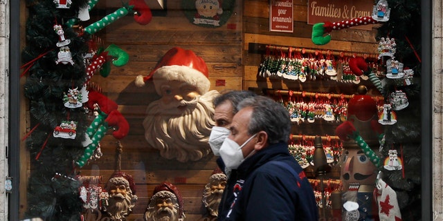 People walk past a shop window adorned with Christmas decorations, in Rome Tuesday, Dec. 1, 2020. Still, the large number of daily new COVID-19 cases is worrying, Italian health experts said, especially with the approach of year-end holidays, which could prompt people to ignore social distancing rules and gather in large numbers to celebrate. (AP Photo/Gregorio Borgia)