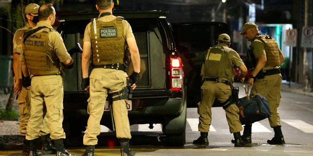 Military police officers carry a bag filled with money left behind by armed bank robbers, in Criciuma, Santa Catarina state, Brazil, Tuesday, Dec. 1, 2020. Dozens of criminals armed with assault rifles invaded the city in southern Brazil overnight and took control of the streets as they assaulted a local bank. (Guilherme Hahn/Futura Press via AP)