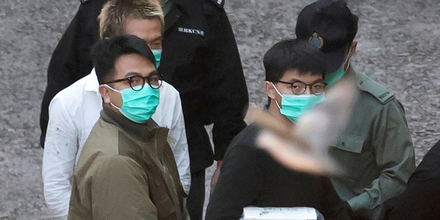 A bird flies as Hong Kong activists Joshua Wong, right, and Ivan Lam, left, are escorted by Correctional Services officers to get on a prison van before appearing in a court, in Hong Kong, Wednesday, Dec. 2, 2020. (AP Photo/Kin Cheung)