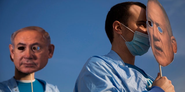 Israeli demonstrators hold masks depicting Israeli Prime Minister Benjamin Netanyahu, left, and Israeli Defense Minister Benny Gantz, right, during a protest against a parliamentary vote to dissolve the Knesset and send the country to its fourth elections in two years while it still hasn't approved a national budget for 2020, in Tel Aviv, Wednesday, Dec. 2, 2020. (AP Photo/Oded Balilty)