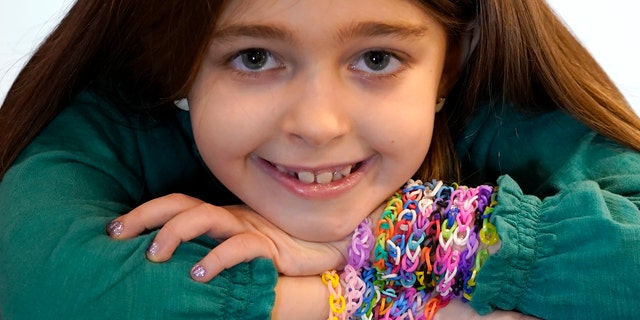 Hayley Orlinsky poses for a portrait Wednesday, Dec. 2, 2020, with several colorful rubber band bracelets she makes in her Chicago home. The 7-year-old has spent most of the coronavirus pandemic crafting the bracelets as a fundraiser, earning nearly $20,000, to buy personal protective equipment for the Ann and Robert H. Lurie Children's Hospital. (AP Photo/Charles Rex Arbogast)