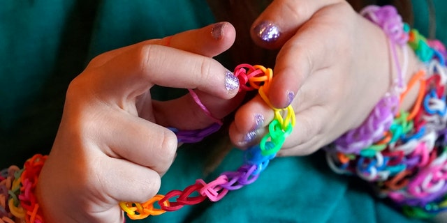 Hayley Orlinsky examines a bracelet she made from colorful rubber bands Wednesday, Dec. 2, 2020, in the bedroom of her Chicago home. The 7-year-old has spent most of the coronavirus pandemic crafting the bracelets as a fundraiser, earning nearly $20,000, to buy personal protective equipment for the Ann and Robert H. Lurie Children's Hospital. (AP Photo/Charles Rex Arbogast)