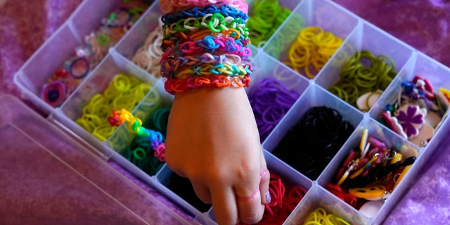 Hayley Orlinsky reaches for a red rubber band Wednesday, Dec. 2, 2020, as she makes a colorful bracelet in the bedroom of her Chicago home. The 7-year-old has spent most of the coronavirus pandemic crafting the bracelets as a fundraiser, earning nearly $20,000, to buy personal protective equipment for the Ann and Robert H. Lurie Children's Hospital. (AP Photo/Charles Rex Arbogast)