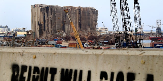 A slogan is painted on a barrier in front of towering grain silos gutted in the massive August explosion at the Beirut port that claimed the lives of more than 200 people, in Beirut, Lebanon, Wednesday, Dec. 2, 2020. (AP Photo/Hussein Malla)