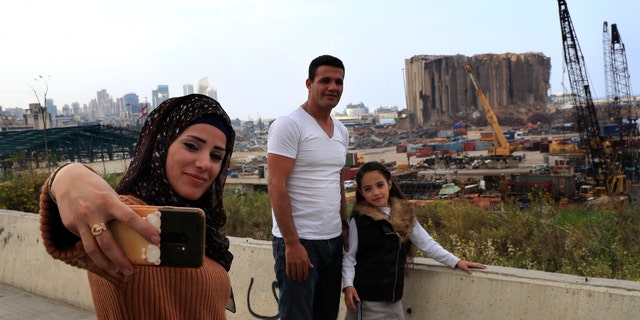 A Lebanese family takes a selfie in front of towering grain silos gutted in the massive August explosion at the Beirut port that claimed the lives of more than 200 people, in Beirut, Lebanon, Wednesday, Dec. 2, 2020. (AP Photo/Hussein Malla)