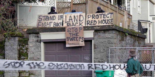 Masked protesters by an occupied home speak with a neighborhood resident opposed to their encampment and demonstration in Portland, Ore., on Wednesday, Dec. 9, 2020. (AP Photo/Gillian Flaccus)
