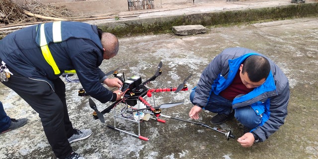 In this Dec. 10, 2020, photo released by Blue Sky Rescue of Zhong County, workers prepare a drone equipped with a flamethrower at a village near Chongqing municipality in southwestern China. (Blue Sky Rescue of Zhong County via AP)