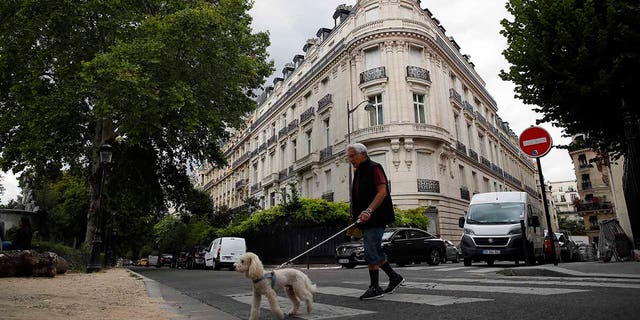 In this Aug.13, 2019 file photo, a man walks his dog next to an apartment building owned by Jeffrey Epstein in Paris. Modeling agent Jean-Luc Brunel who was close to U.S. financier Jeffrey Epstein has been taken into custody in France, suspected of an array of crimes, including the rape of minors and trafficking minors for sexual exploitation, Paris prosecutors said Thursday.(AP Photo/Francois Mori, File)