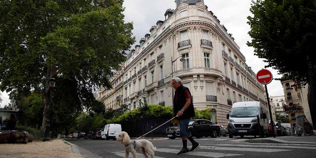 In this Aug.13, 2019 file photo, a man walks his dog next to an apartment building owned by Jeffrey Epstein in Paris. Modeling agent Jean-Luc Brunel who was close to U.S. financier Jeffrey Epstein has been taken into custody in France, suspected of an array of crimes, including the rape of minors and trafficking minors for sexual exploitation, Paris prosecutors said Thursday.(AP Photo/Francois Mori, File)