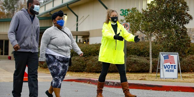 An Election Defender volunteer directs voters to an area where they can get free hand sanitizer and masks during early voting for the Senate runoff election at a recreation center Thursday, Dec. 17, 2020, in Powder Springs, Ga. (AP Photo/Todd Kirkland)
