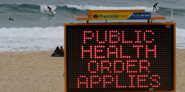Surfers ride a wave past a sign at a beach in Sydney, Australia, Saturday, Dec. 19, 2020.  (AP Photo/Mark Baker)