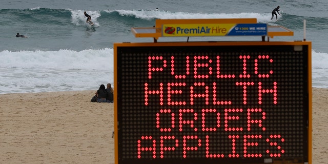 Surfers ride a wave past a sign at a beach in Sydney, Australia, Saturday, Dec. 19, 2020.  (AP Photo/Mark Baker)