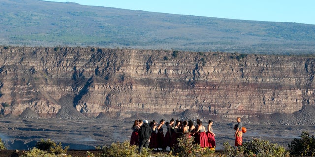 FILE - In this April 25, 2019, photo, a group of Native Hawaiians stand next to the collapsed caldera floor of Kilauea volcano in Hawaii Volcanoes National Park on the Big Island. The U.S. Geological Survey says the Kilauea volcano on Hawaii’s Big Island has erupted. The eruption began late Sunday, Dec. 20, 2020 within the Halema’uma’u crater. The volcano is located within Hawaii Volcanoes National Park. (AP Photo/Caleb Jones, File)