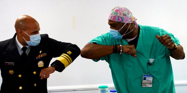 Surgeon General of the U.S. Jerome Adams, left, elbow-bumps Emergency Room technician Demetrius Mcalister after Mcalister got the Pfizer COVID-19 vaccination at Saint Anthony Hospital in Chicago, on Tuesday, Dec. 22, 2020. (Youngrae Kim/Chicago Tribune via AP, Pool)