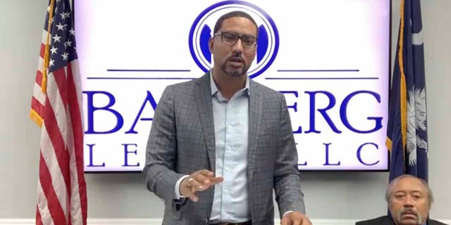 In this screengrab from video provided by Bamberg Law, LLC, attorney Justin Bamberg, standing, speaks at a news conference as plaintiff Jethro DeVane, seated at right, listens, Tuesday, Dec. 22, 2020, in Orangeburg, S.C. (Courtesy of Bamberg Law, LLC via AP)