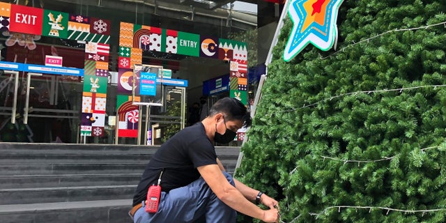 A worker wearing a face mask to help prevent the spread of coronavirus prepares an artificial Christmas tree outside a shopping mall that would normally be busy with foreign tourists in Bangkok on Wednesday, Dec. 23, 2020. Thailand has kept the coronavirus largely in check for most of the year but is facing a challenge from a large outbreak that threatens to undo months of efforts to contain the virus and hasten recovery of an ailing economy that relies heavily on tourism.(AP Photo/Adam Schreck)