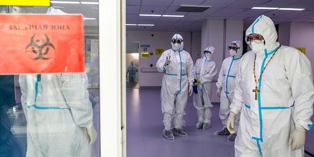 A Russian Orthodox Church priest, right, leaves a red zone after visiting patients suspected of having coronavirus at a hospital in Kommunarka, outside Moscow, Russia, Monday, Dec. 28, 2020. (Sophia Sandurskaya, Moscow News Agency photo via AP)