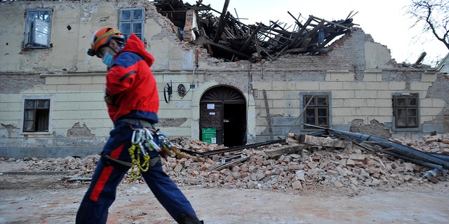 A rescuer walks past a building damaged in an earthquake in Petrinja, Croatia, Tuesday, Dec. 29, 2020. A strong earthquake has hit central Croatia and caused major damage and at least one death and some 20 injuries in the town southeast of the capital Zagreb. (AP Photo)