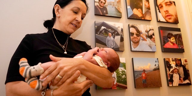 Mercedes Lemp poses for The Associated Press by holding her 2-day-old grandson near portraits of the newborn's father, Duncan Lemp, Vrydag, Okt.. 16, 2020, in Frederick, Md. The Lemp's are dealing with the death of their Duncan Lemp, who was shot at their home in Potomac, Md., during a no-knock police raid on March 12, 2020. Lemp's family have said through their attorney that, based on an eyewitness, they believe Lemp was shot without warning while he was asleep. (AP Foto / Julio Cortez)