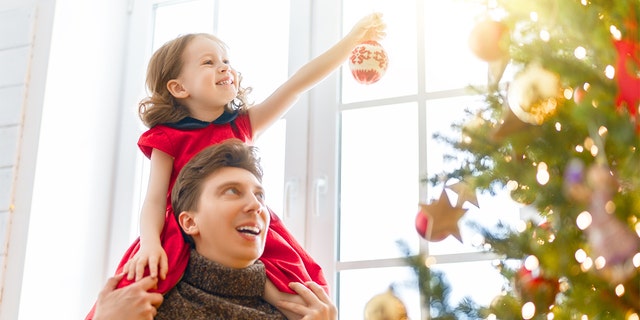 Merry Christmas and Happy Holidays! Dad and daughter near the tree indoors. The morning before Xmas. Portrait loving family close up.