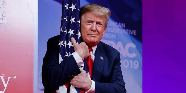 President Donald Trump hugs the American flag as he arrives to speak at the Conservative Political Action Conference, CPAC 2019, in Oxon Hill, Md., on March 2, 2019. Trump again hugged an American flag as he began his address to CPAC 2021. (AP Photo/Carolyn Kaster)