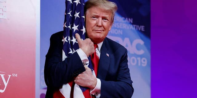 President Donald Trump hugs the American flag as he arrives to speak at the Conservative Political Action Conference, CPAC 2019, in Oxon Hill, Md., on March 2, 2019. (AP Photo/Carolyn Kaster)