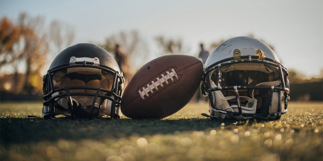 American football helmets and ball on the playing field, no people.