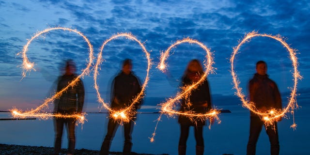 Four people write the year 2020 with sparklers into the evening sky at the stand of the Baltic Sea island of Rügen (shot with long time exposure). (Photo by Patrick Pleul/picture alliance via Getty Images)