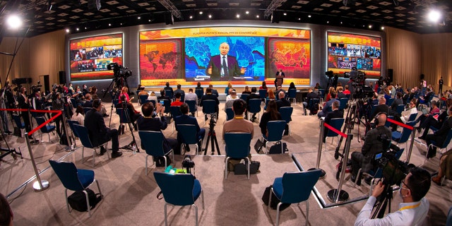 Russian President Vladimir Putin gestures as he speaks via video call during a news conference as journalists wearing face masks to protect against coronavirus, observe social distancing guidelines watch him at a big screen in Moscow, Russia, Thursday, Dec. 17, 2020. This year, Putin attended his annual news conference online due to the coronavirus pandemic. (AP Photo/Alexander Zemlianichenko)