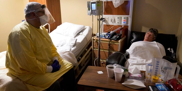 Dr. Shane Wilson, left, sits on a bed as he talks with COVID-19 patient JoBeth Harvey, who used to be a gym teacher at his school.