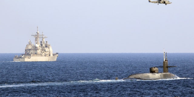 The guided-missile submarine USS Georgia, right, transits the Strait of Hormuz with the guided-missile cruiser USS Port Royal, the guided-missile cruiser USS Philippine Sea, not pictured, and a MH-60R Sea Hawk helicopter, attached to Helicopter Maritime Strike Squadron 48. (U.S. Navy photo by Mass Communication Specialist 2nd Class Indra Beaufort)