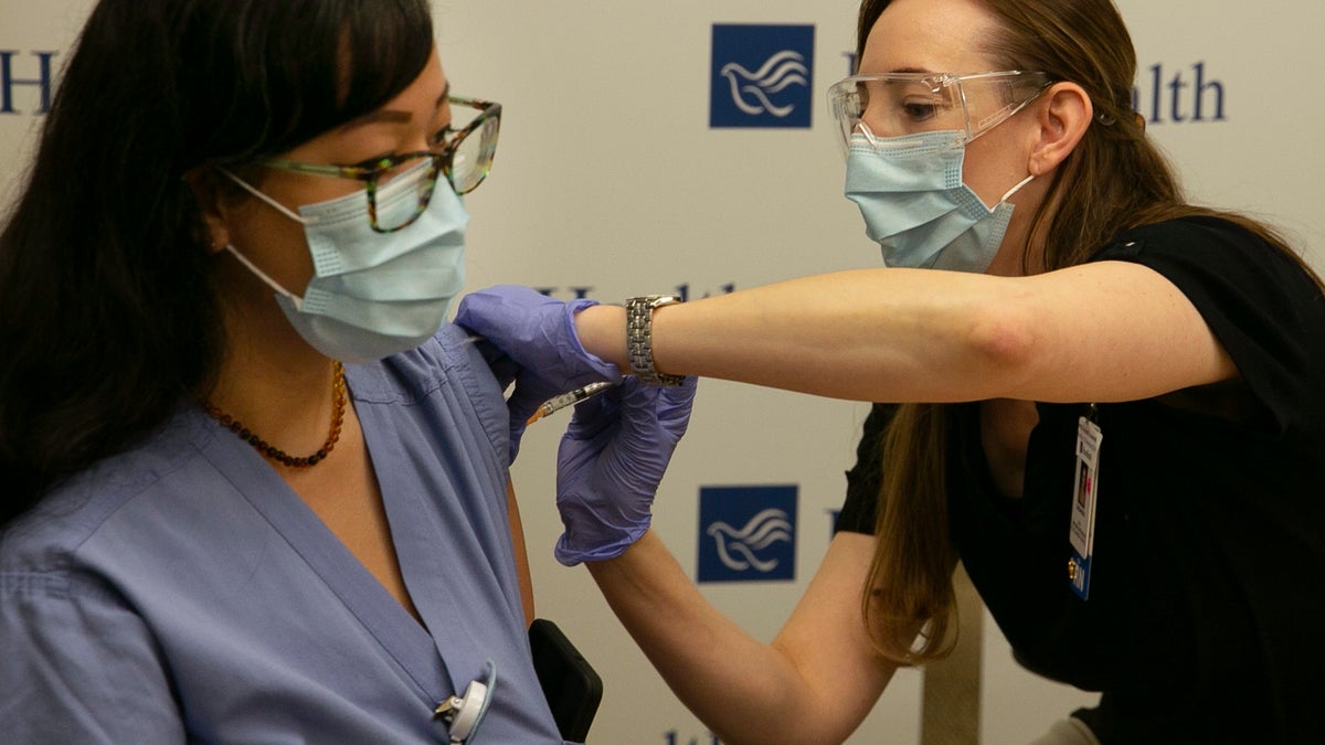 Registered nurse Carol Eickmeyer, left, gets the first vaccination for the coronavirus from RN Cassandra Antosz at Sacred Heart RiverBend Hospital in Springfield, Ore. Monday Dec. 21, 2020. (Chris Pietsch/The Register-Guard via AP, Pool)
