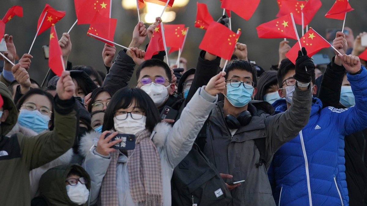 In this photo released by Xinhua News Agency, visitors to Tiananmen Square wave Chinese national flags as they attend the flag raising ceremony on Tiananmen Square in Beijing Friday, Jan. 1, 2021. (Ju Huanzong/Xinhua via AP)